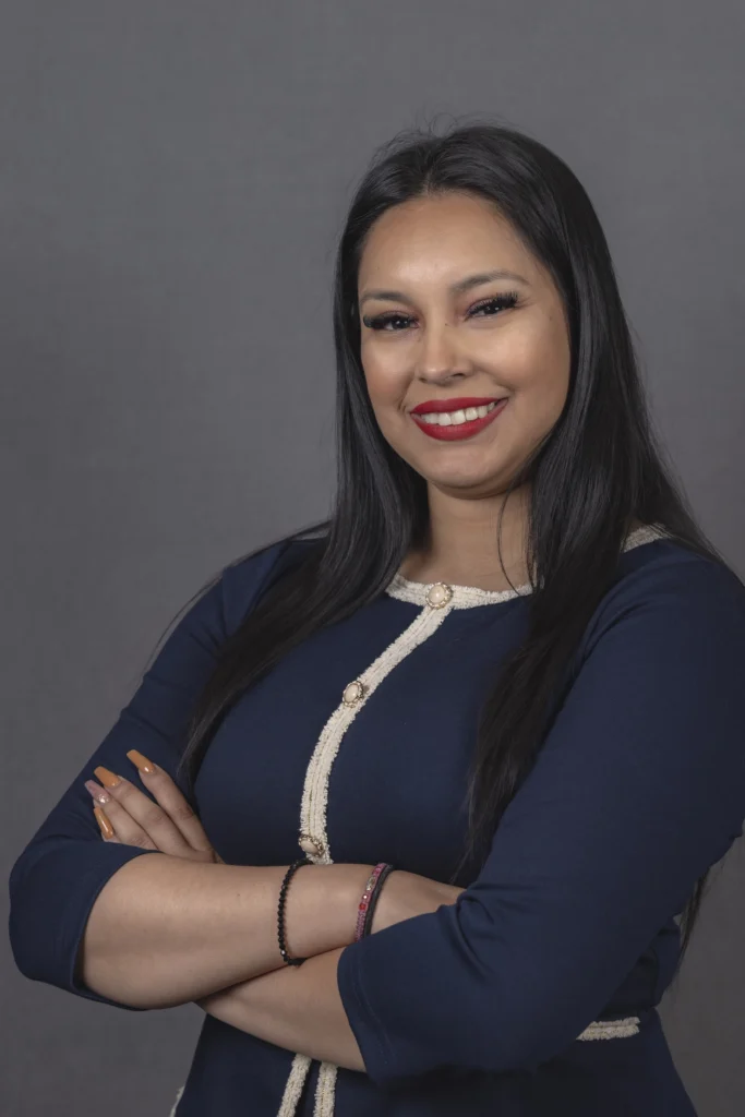 Young professional woman in a blue blazer smiling, studio headshot on dark background, Portland