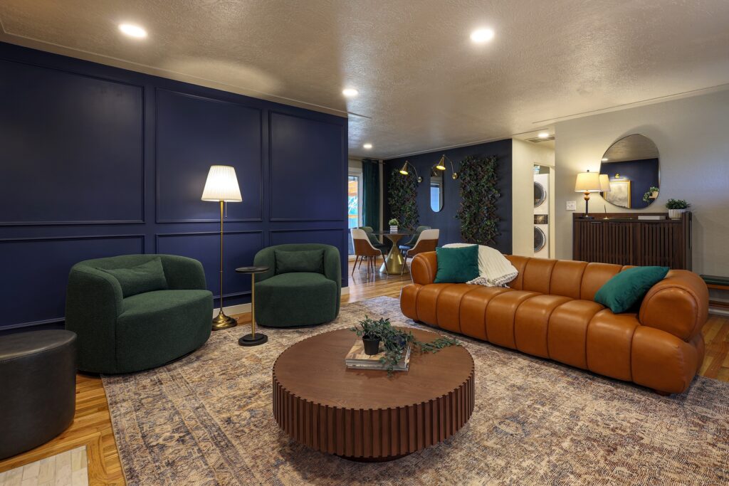 Modern living room interior with dark blue paneled wall, orange leather sofa, and green armchairs