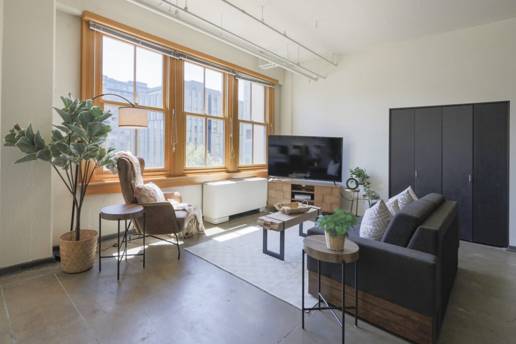 Bright industrial loft living room with large windows, natural light, and city views