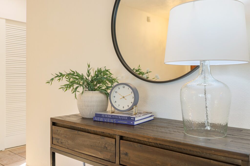 Interior decor detail featuring a round mirror, modern clock, and books on a wooden console table.