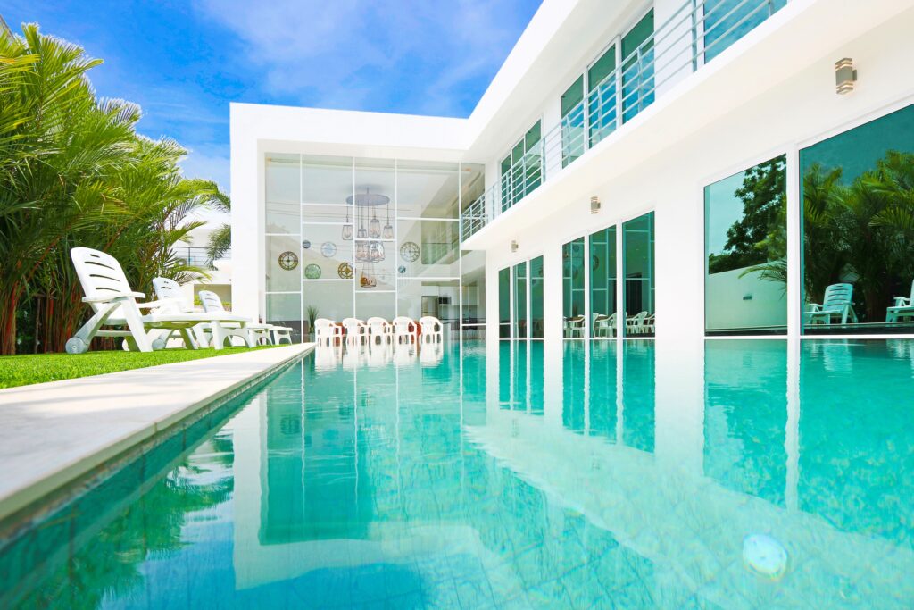 Luxury modern villa with a large infinity swimming pool, white sun loungers, and bright blue sky.