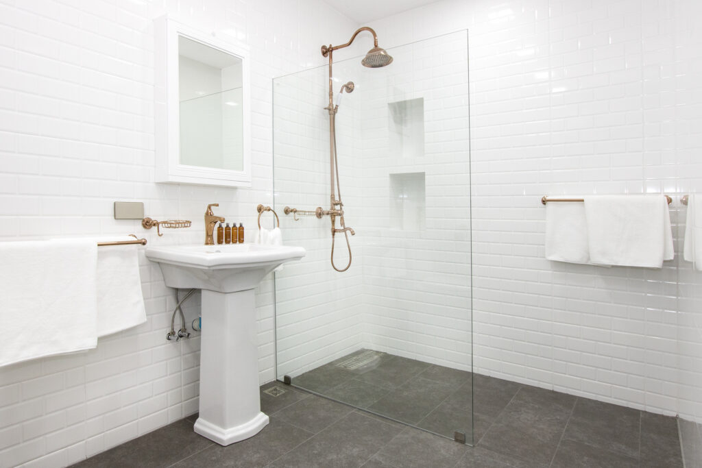 Clean and bright bathroom interior with white subway tiles, glass shower door, and gold hardware fixtures.